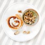 Cinnamon roll and nuts on a white plate.