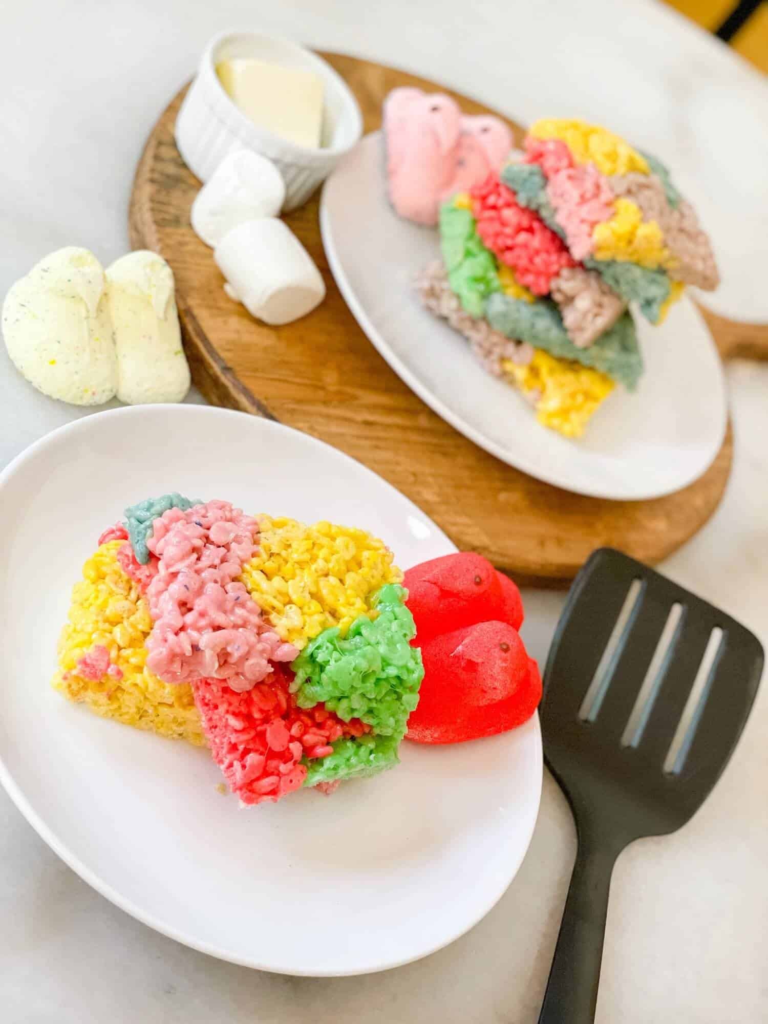 Colorful Rice Krispie Treats on a white plate next to a spatula.