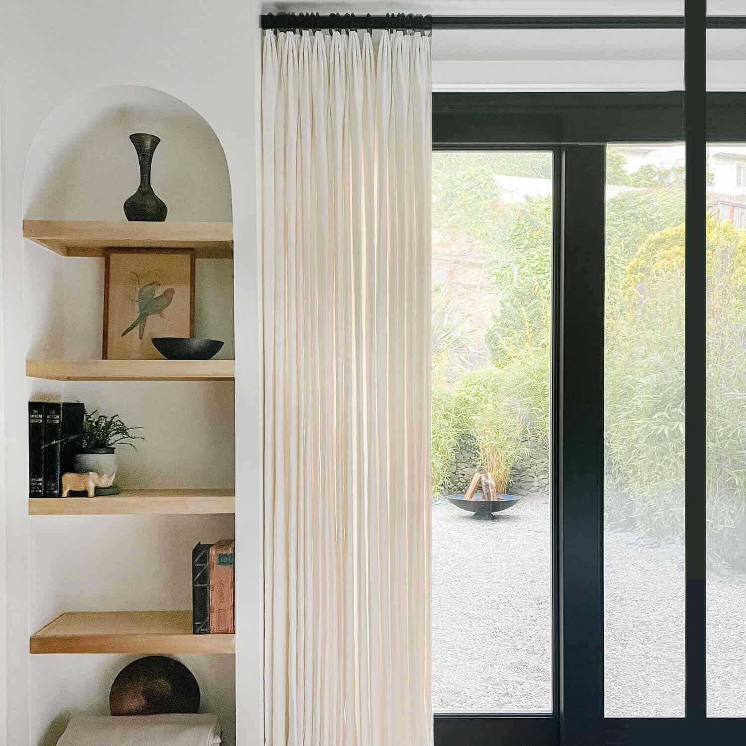 White curtain hanging to the side of a window looking onto a fire bowl.