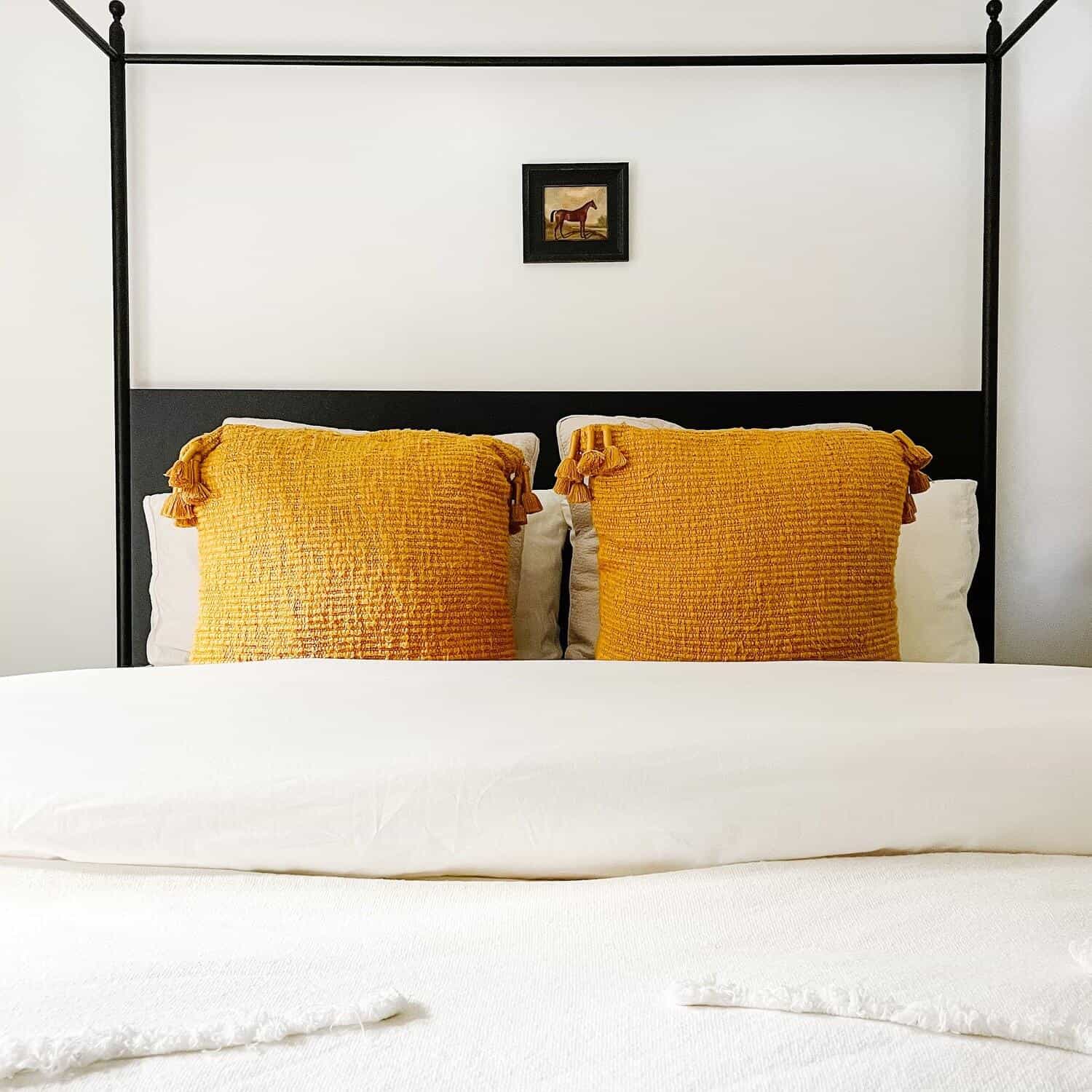 Two saffron tassel throw pillows on a bed.