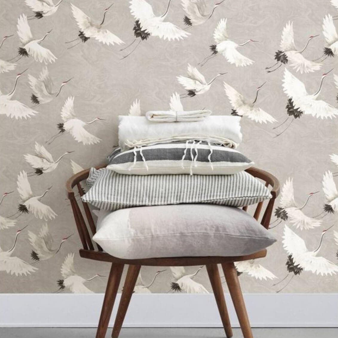 Grey and white bird wallpaper behind a chair stacked with pillows.