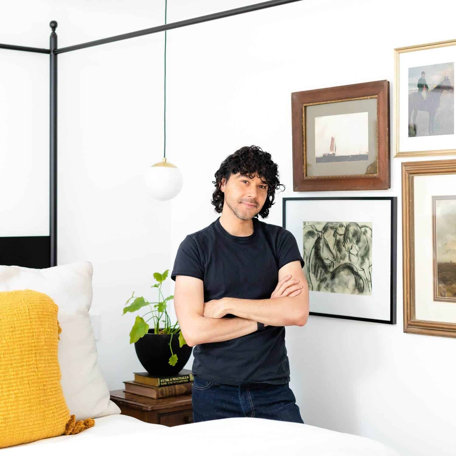 Anthony standing between a bed and a gallery wall.