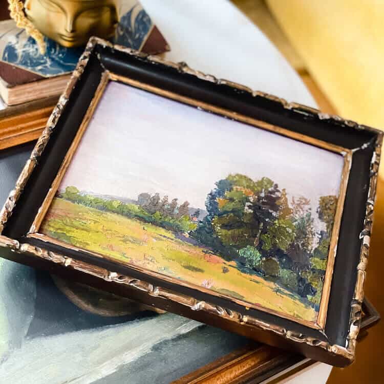 Framed landscape picture on a pile of art.