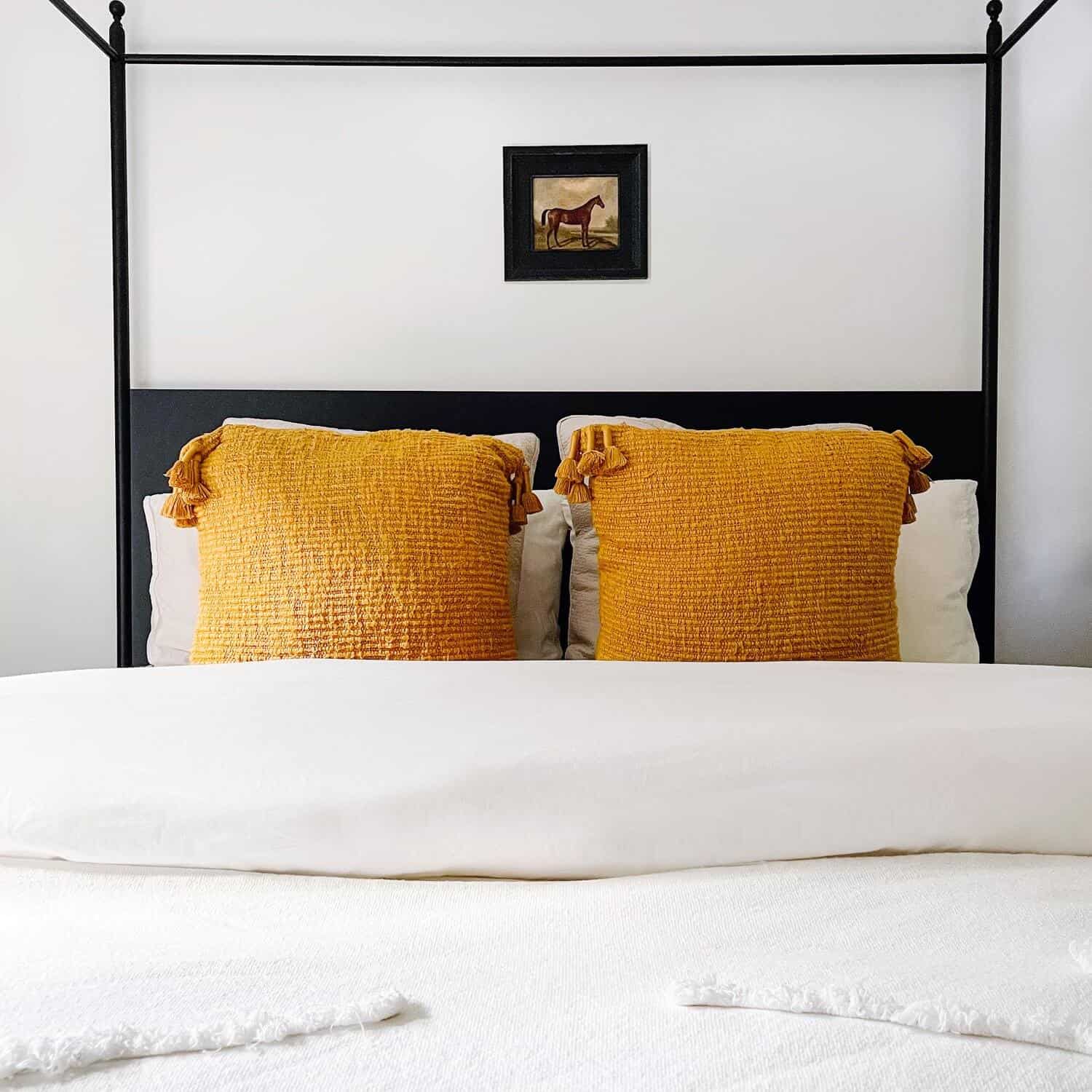 Orange tasseled throw pillows on a white bed.