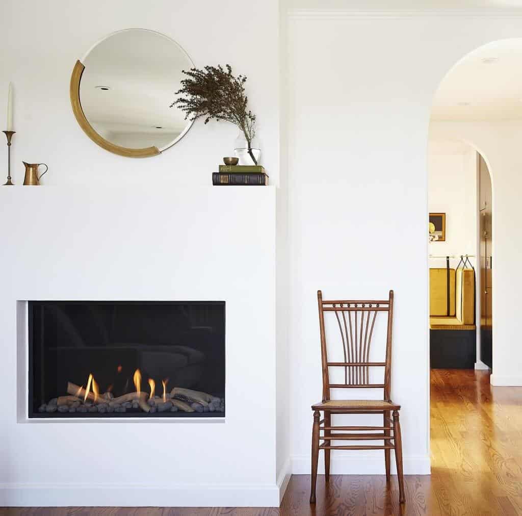 Crescent mirror on a white wall over a fireplace.