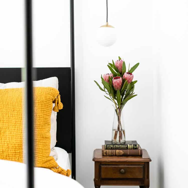 Mustard throw pillows pair with vintage books, and a Facebook Marketplace nightstand and ceiling mounted pendant light