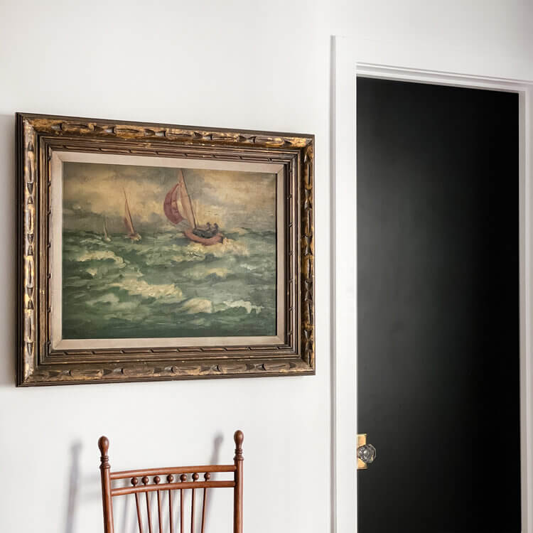 A Vintage storm at sea painting juxtaposes nicely with a garage sale chair and modern black paint with brass and crystal