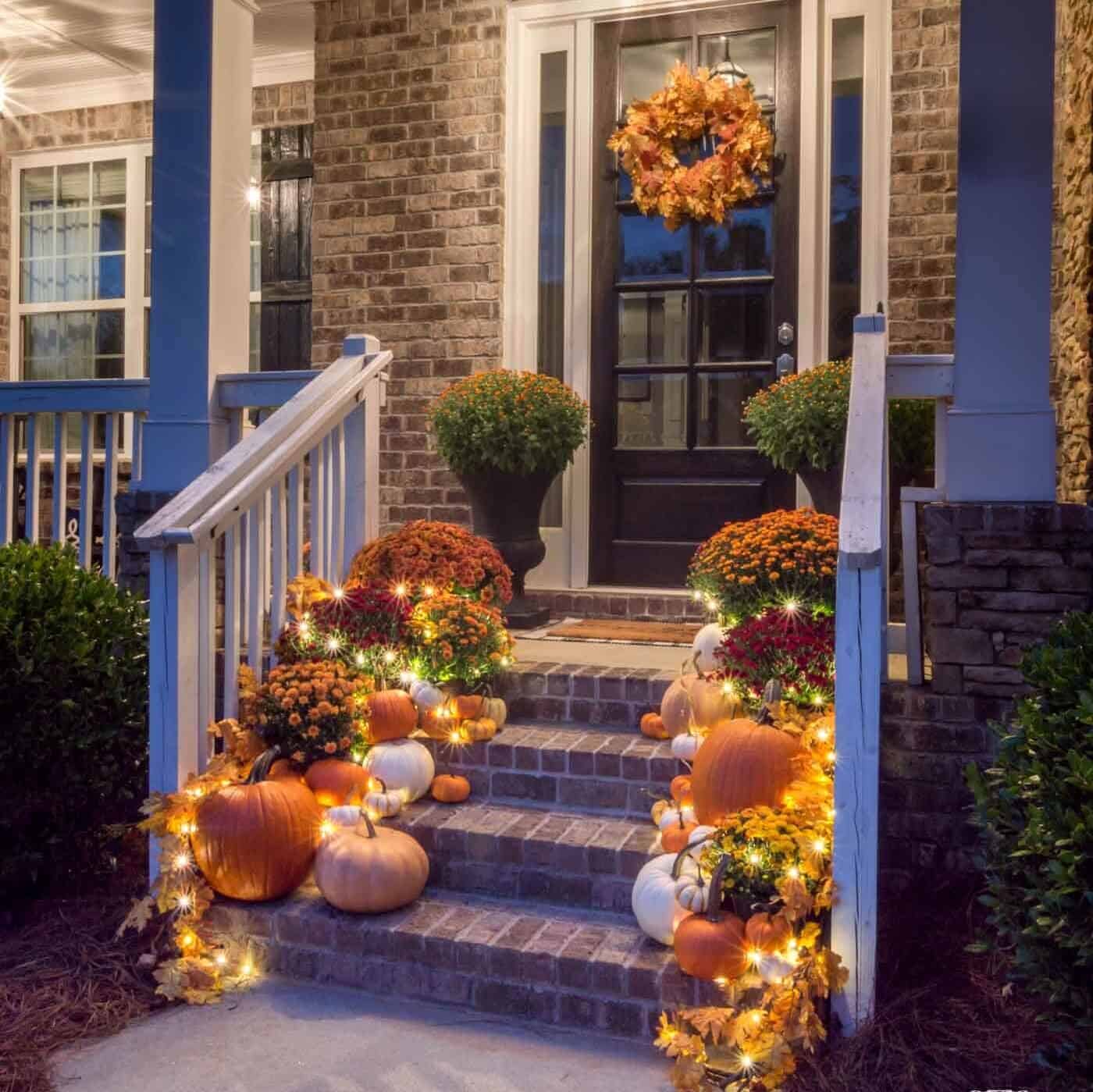 Pumpkins, mums, and lights on brick steps.
