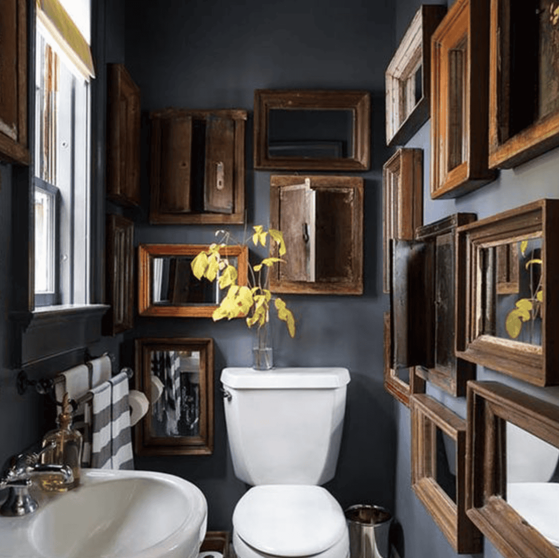 Several mirrors and cabinets on dark walls in a small bathroom.