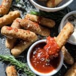 Mozzarella stick being dipped in marinara sauce from a small bowl.