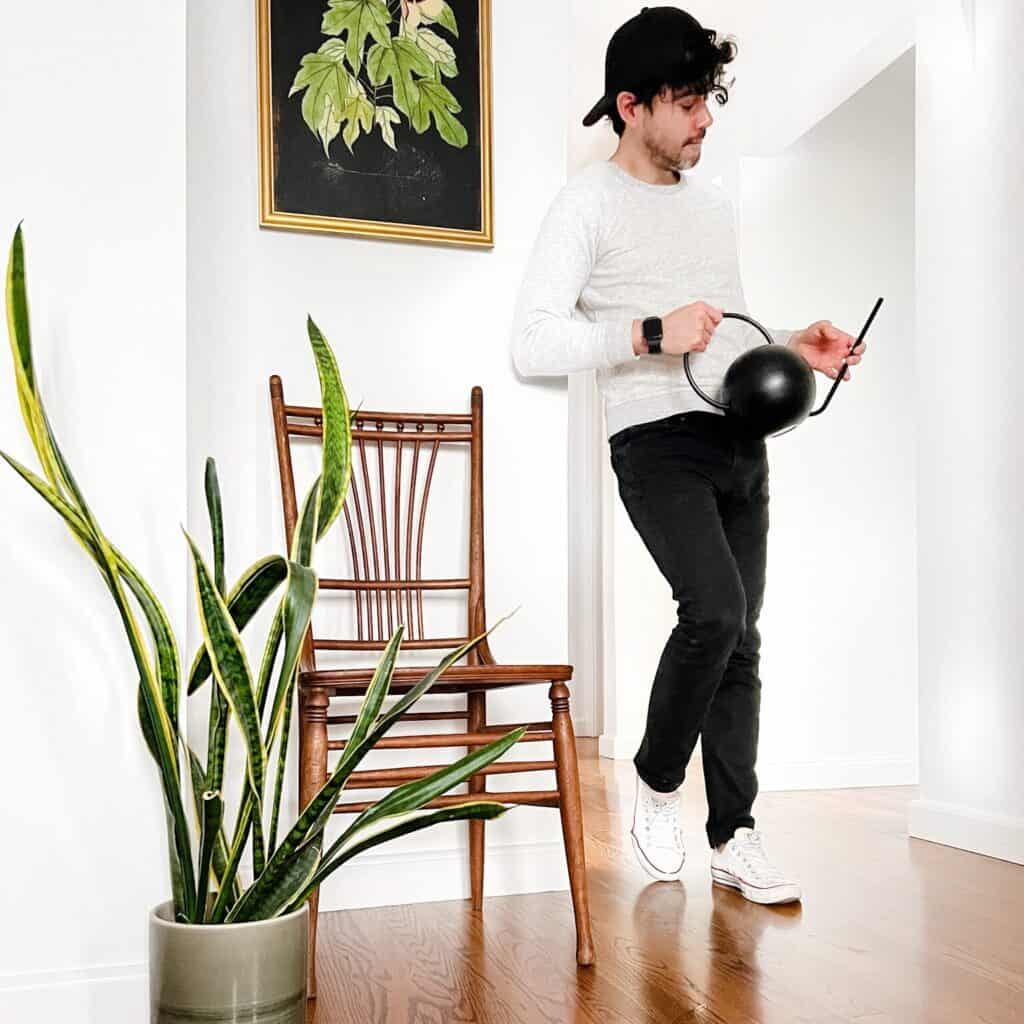 Man holding a watering can in a room with a plant.