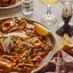 Plate of lobster ravioli on a table with candles and lemon wedges.