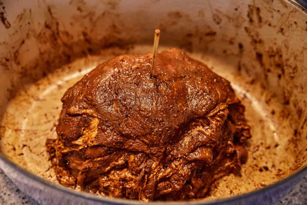 Slices of pork on a skewer in a Dutch Oven.