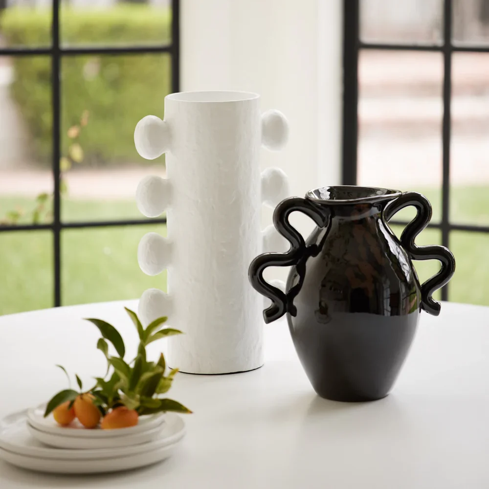 Black vase with curvy handles on a white table.