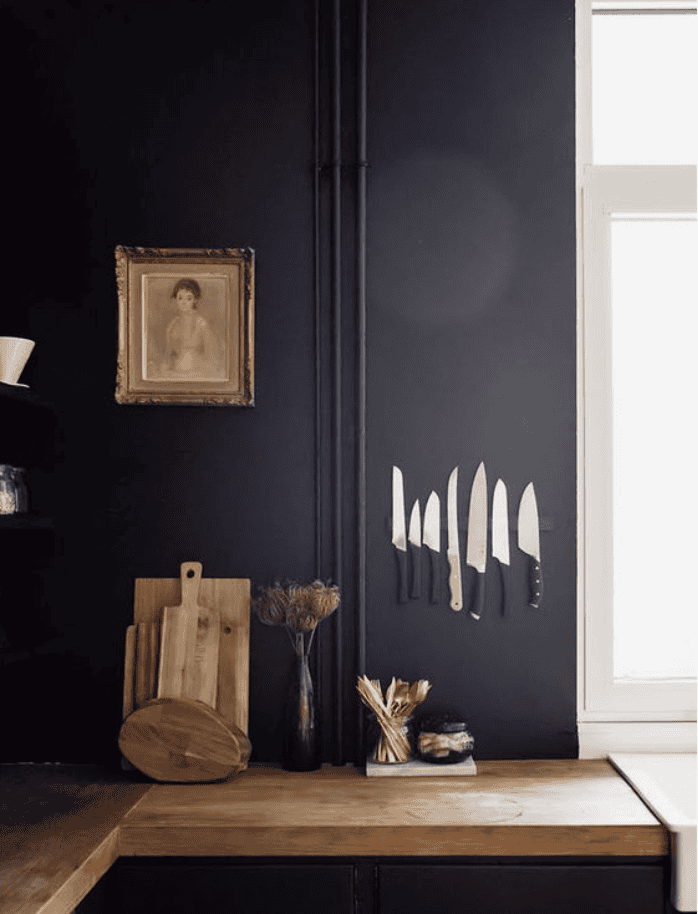Black wall with a knives hanging from a magnetic strip and a tan picture of a woman.