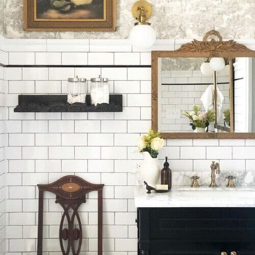 Bathroom with white subway tiles, a wooden chair, and gold accents.