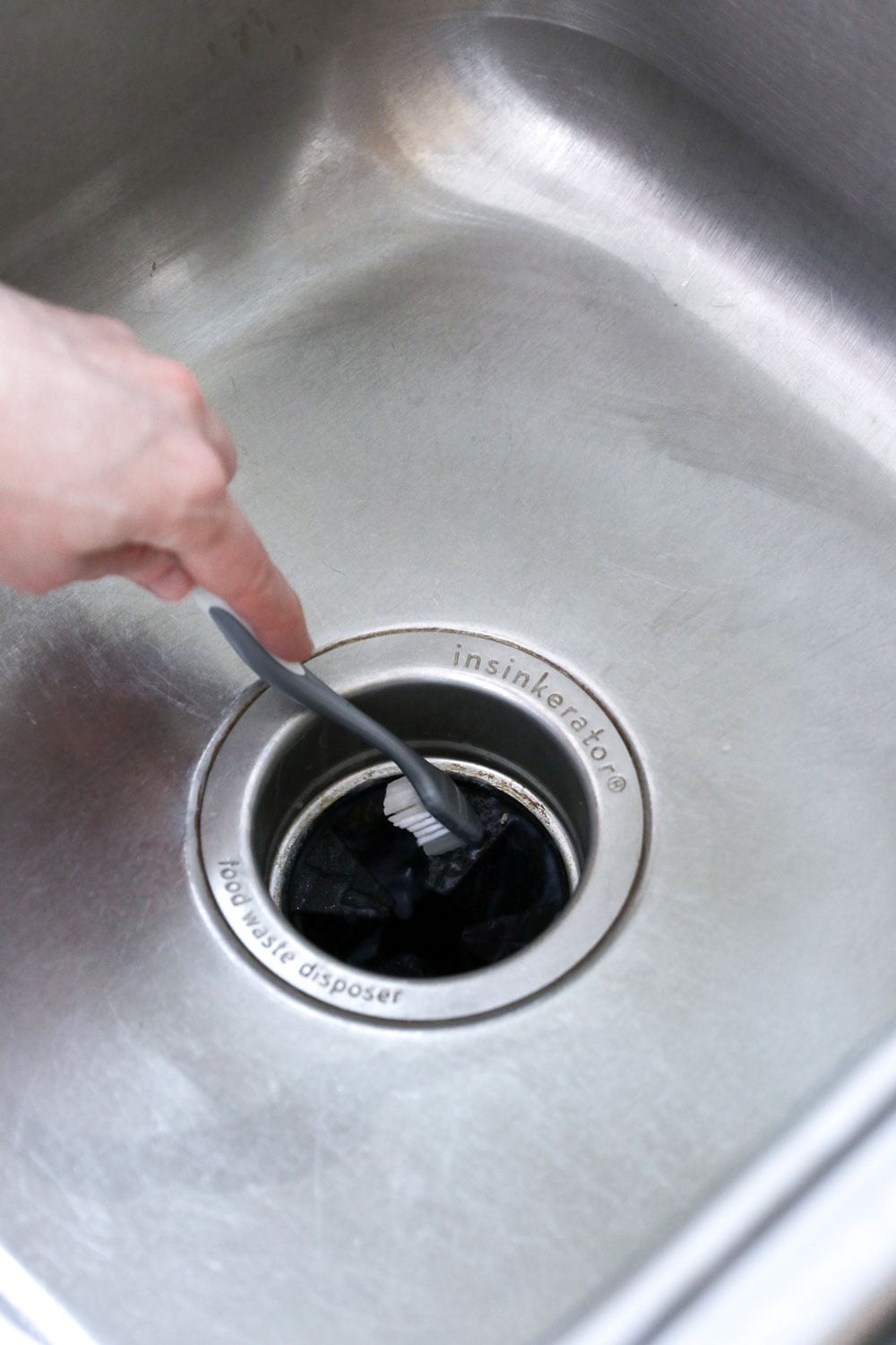 Person cleaning a sink drain with a toothbrush.