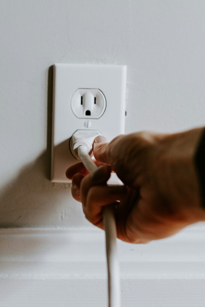 Person plugging a cord into a wall.