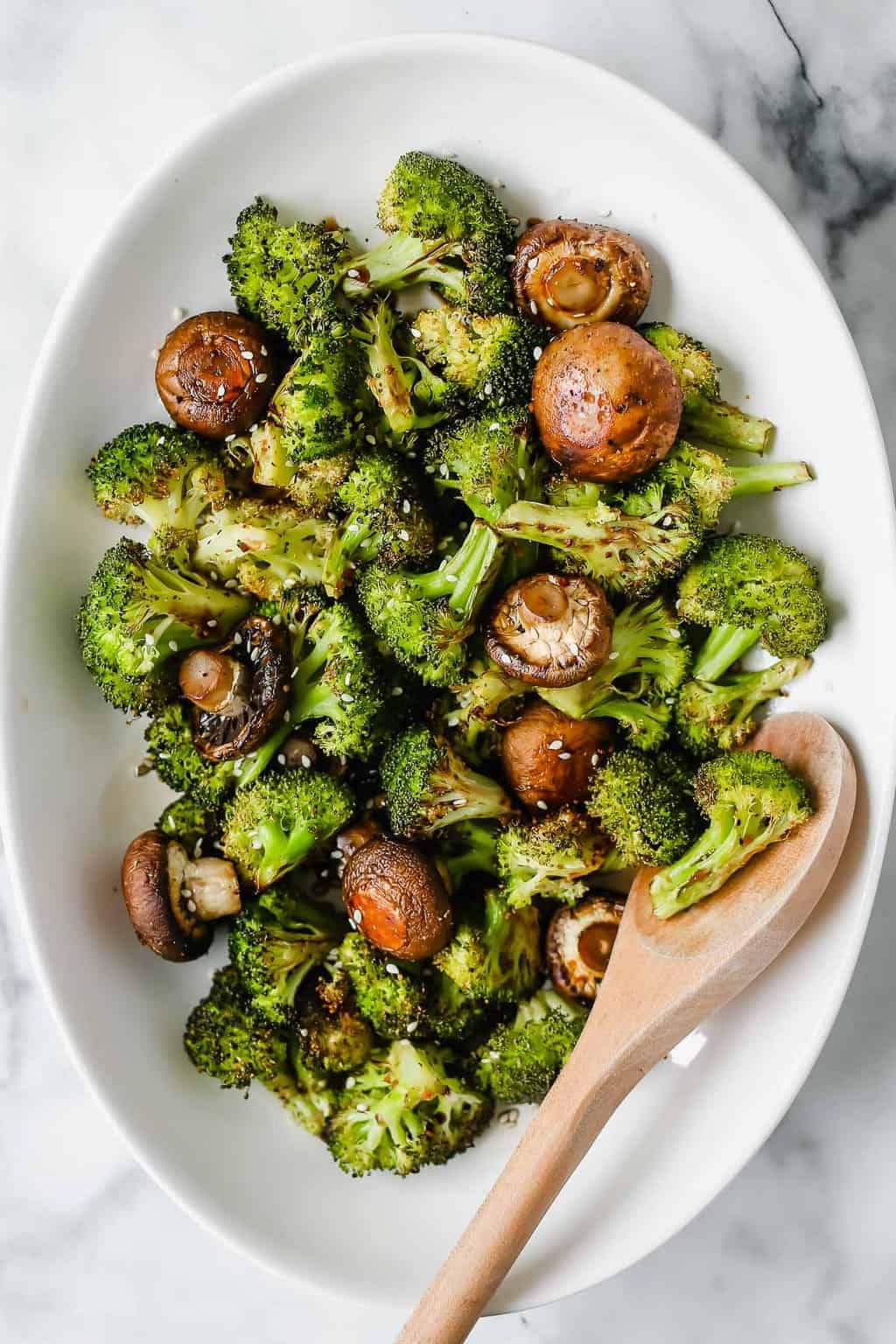 Spoon in a dish of roasted broccoli and mushrooms.