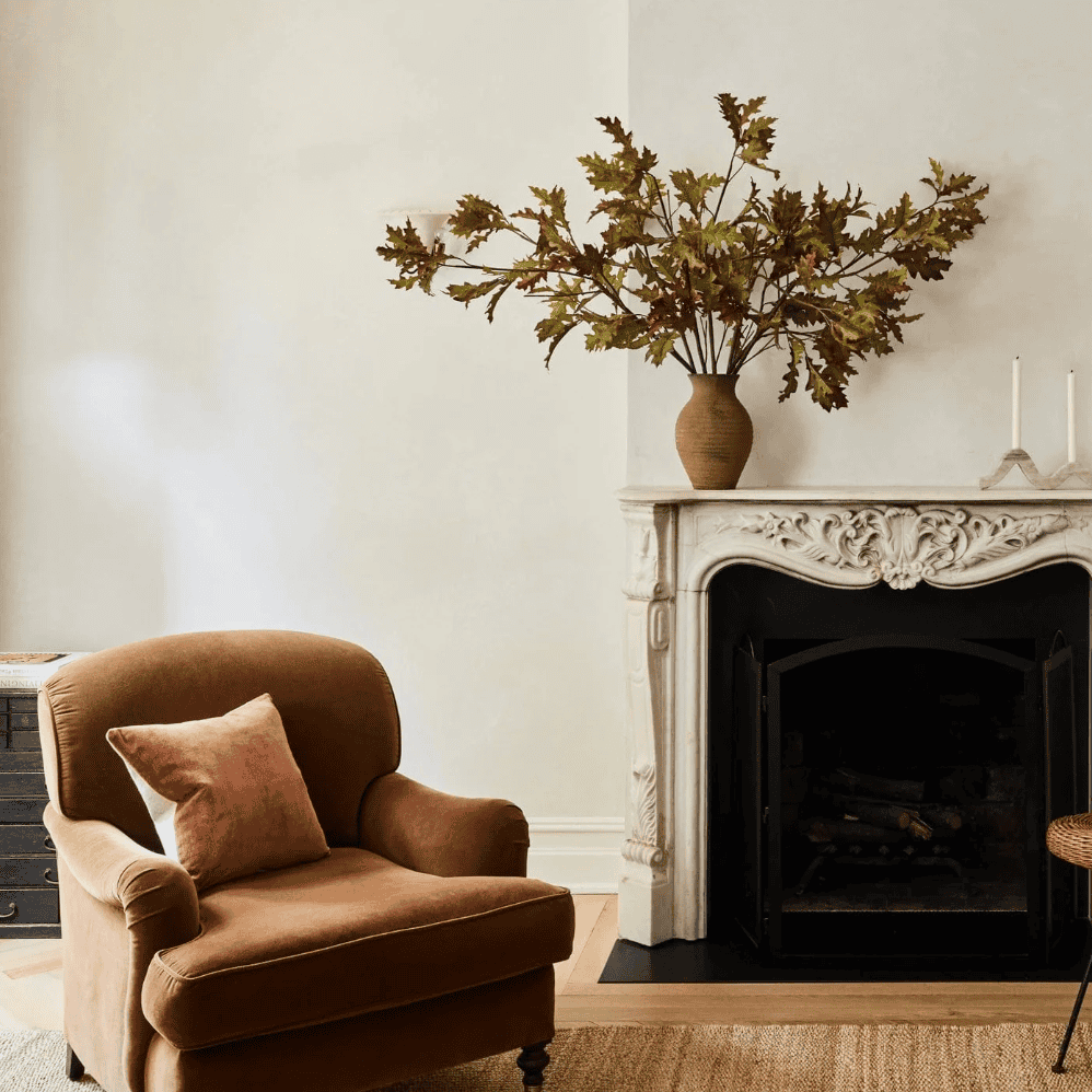 Oak leaf branch in a brown vase on a mantle.