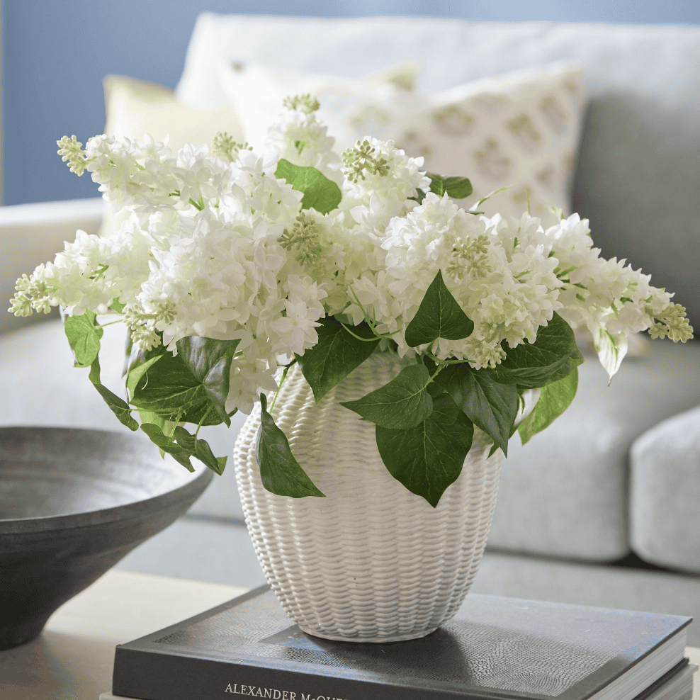 White, fake lilacs in a white wicker vase.