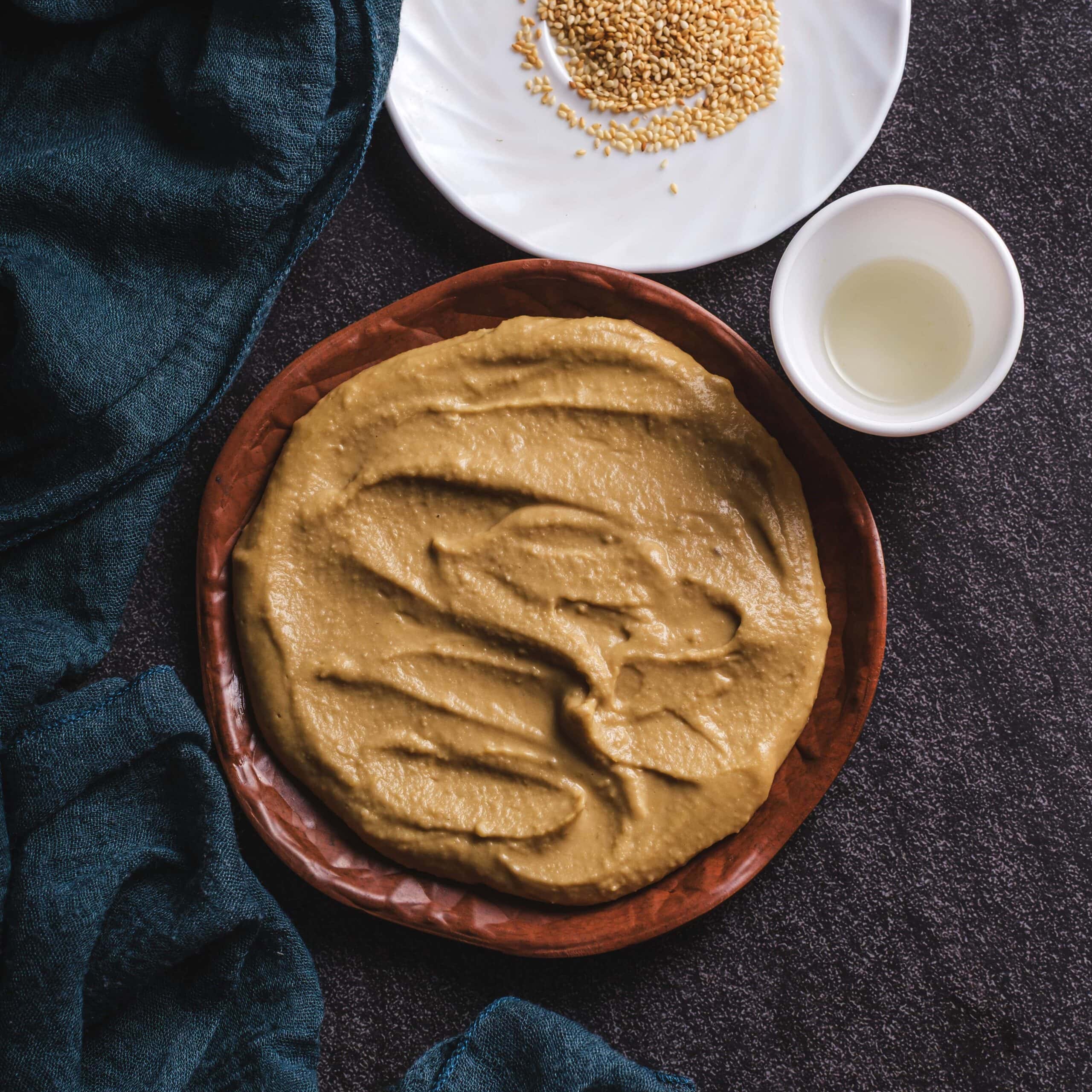 a stunning miso mayo on a black table with a blue napkin and a plate of sesame seeds.  