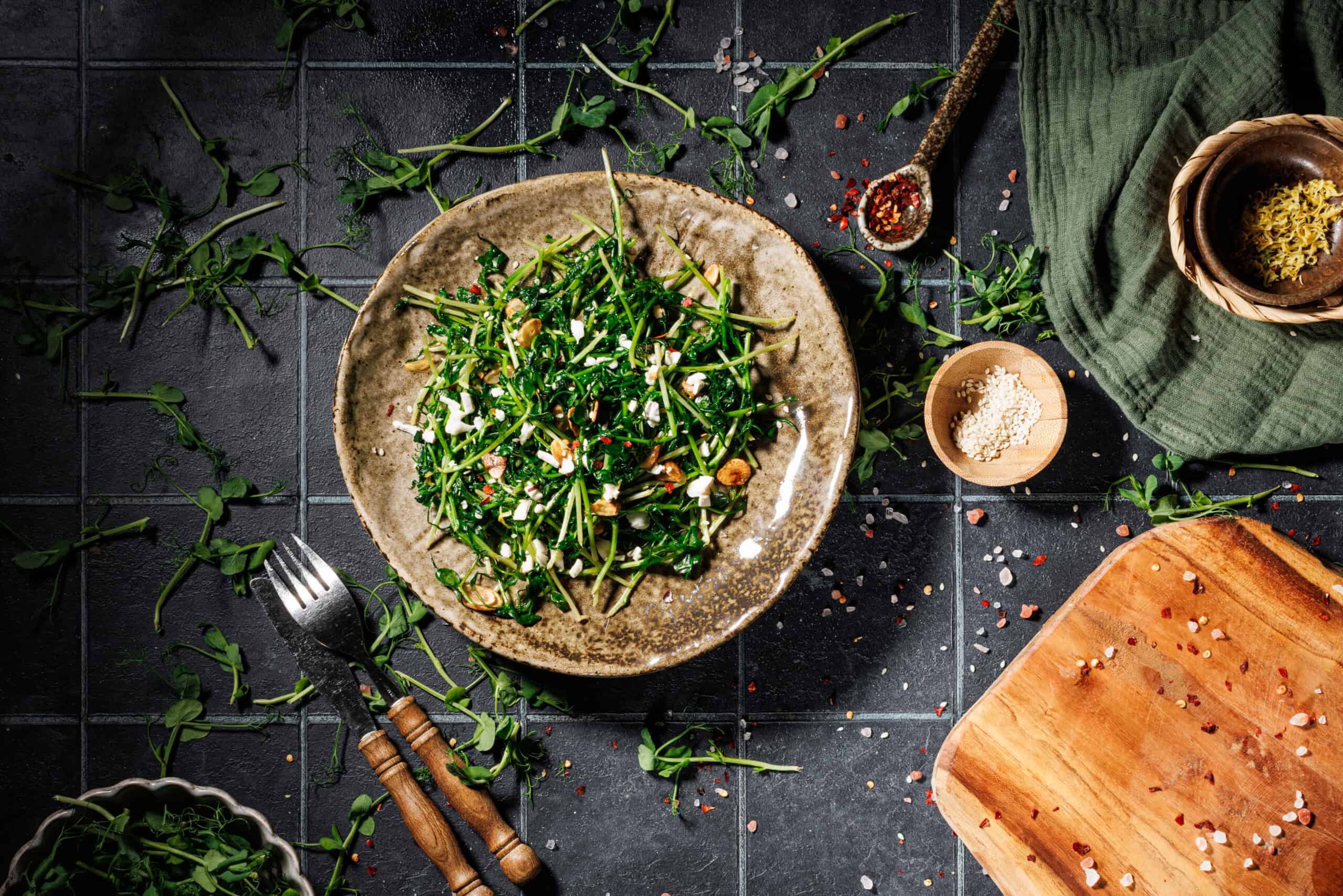 Sautéed pea shoots plated and garnished with crispy garlic, crumbled goat cheese, and a sprinkle of red pepper flakes.
