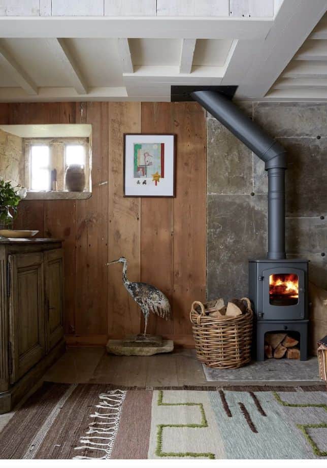 Restored cabin interior featuring the best wood stove for cabin heating with a concrete surround, modern frame, and knit rug with a bird statue.

