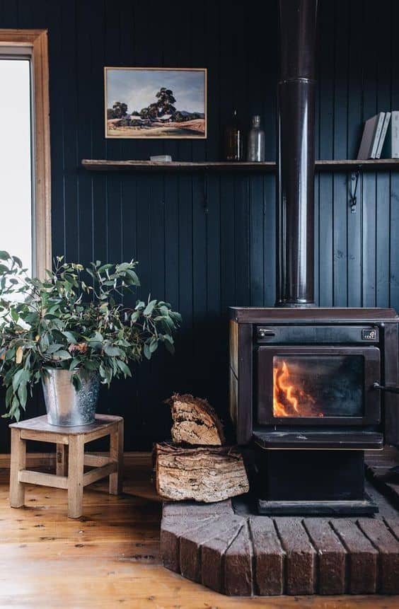 A vintage wood-burning stove on brick, with a black board and batten wall, and a vintage painting.
