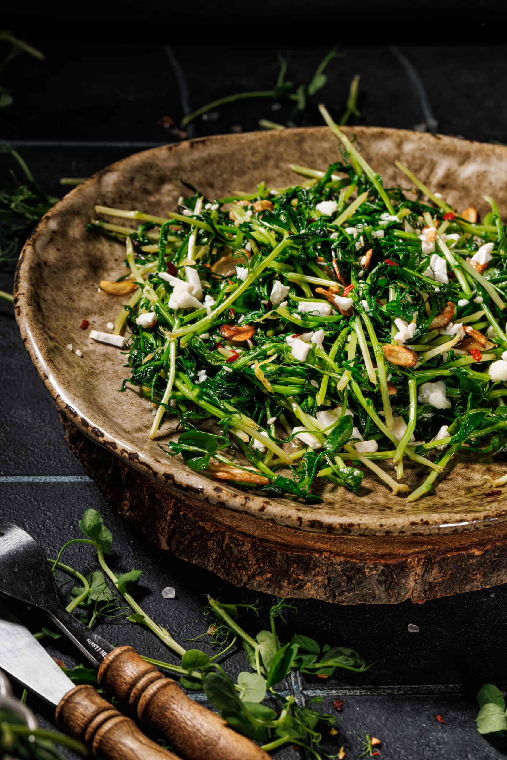 Sautéed pea shoots on a ceramic plate topped with crispy garlic and creamy goat cheese.