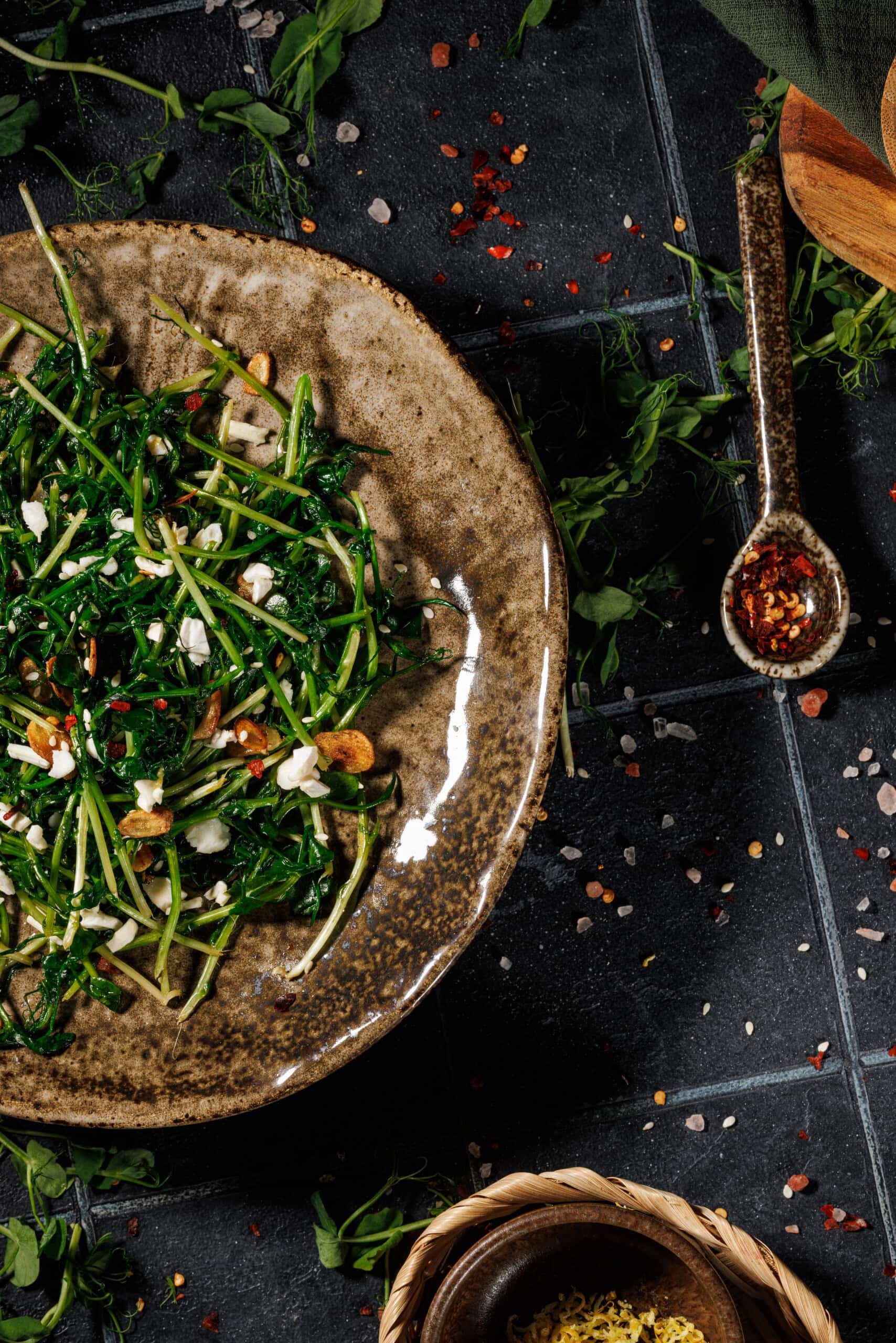 close up offreshly prepared  pea shoots plated and garnished  with red chili flakes, salt, and crispy garlic.