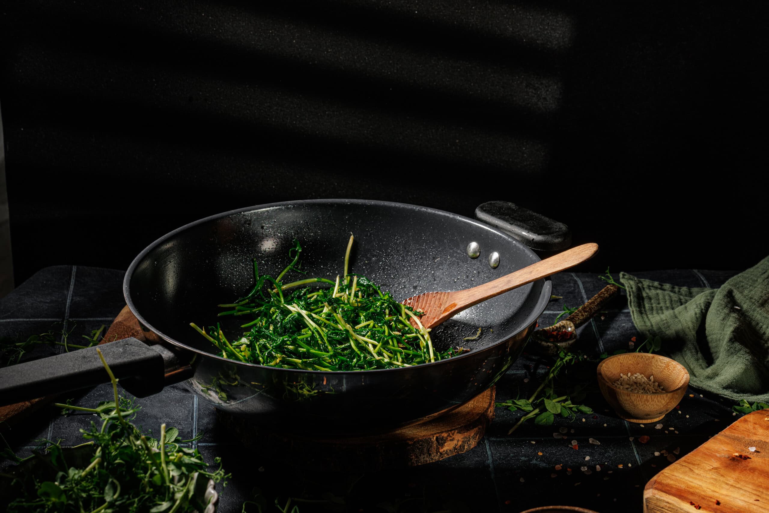 Bright green pea shoots in a skillet, lightly tossed with sesame oil and lemon zest.