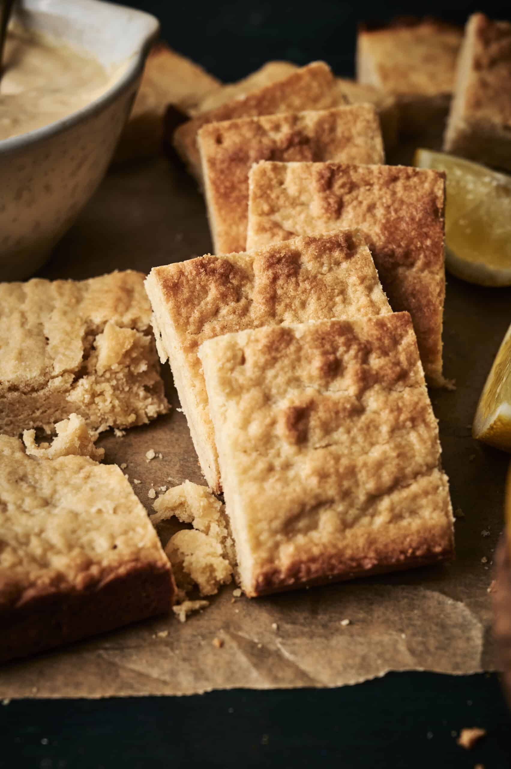 Golden lemon cookie bars stacked with crumbling squares on parchment paper  and fresh lemon zest.