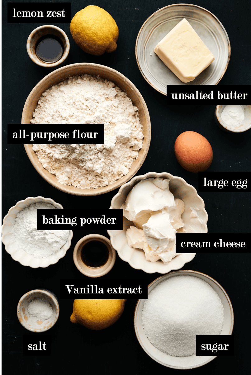 ingredients on a black table to make lemon cookie bars with cream cheese swirl including; lemon, floour, an egg, vanilla extract, and cream cheese etc.