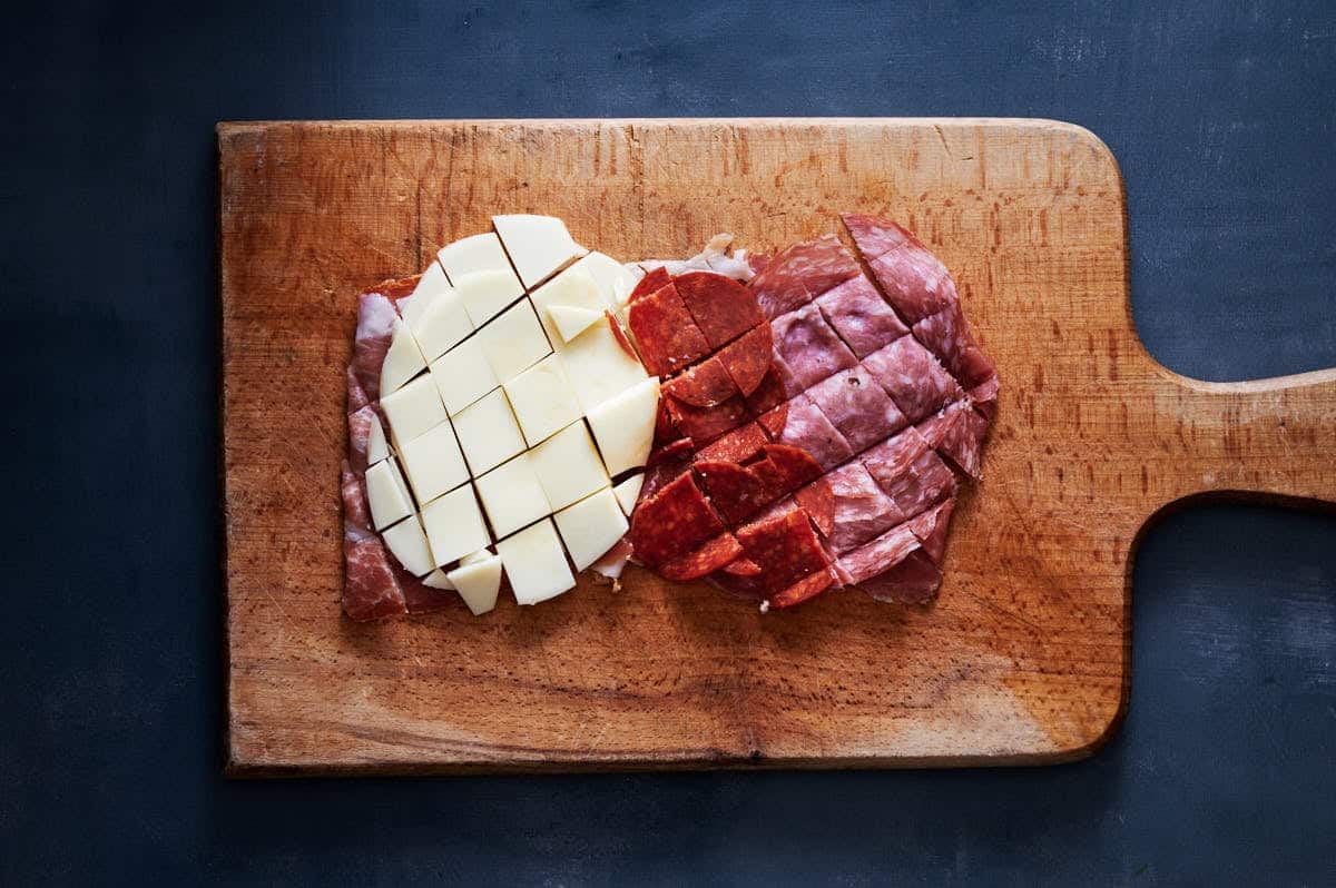 chopped Italian sandwich meat sliced with cheeses on a wooden cutting board.