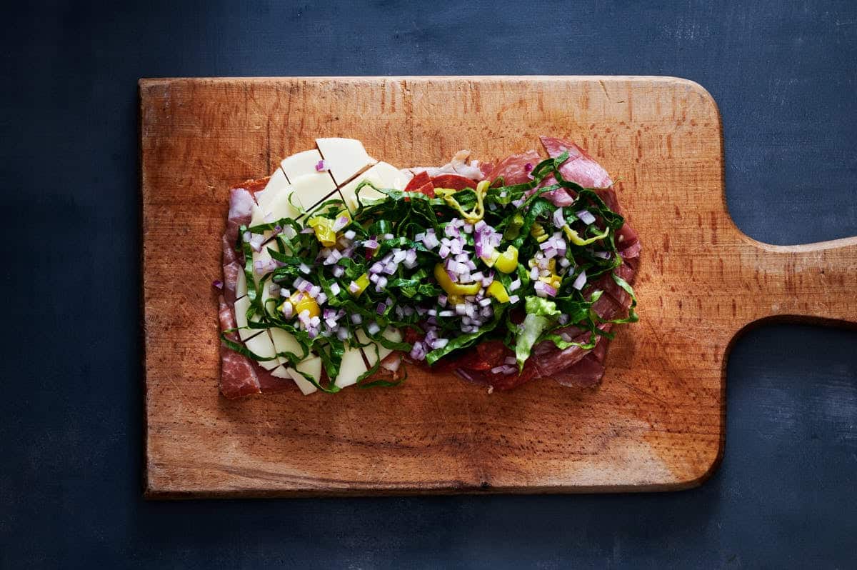 All the meat, cheese, and salad mixes are thinly sliced and diced on a table to make a chopped italian sandwich.