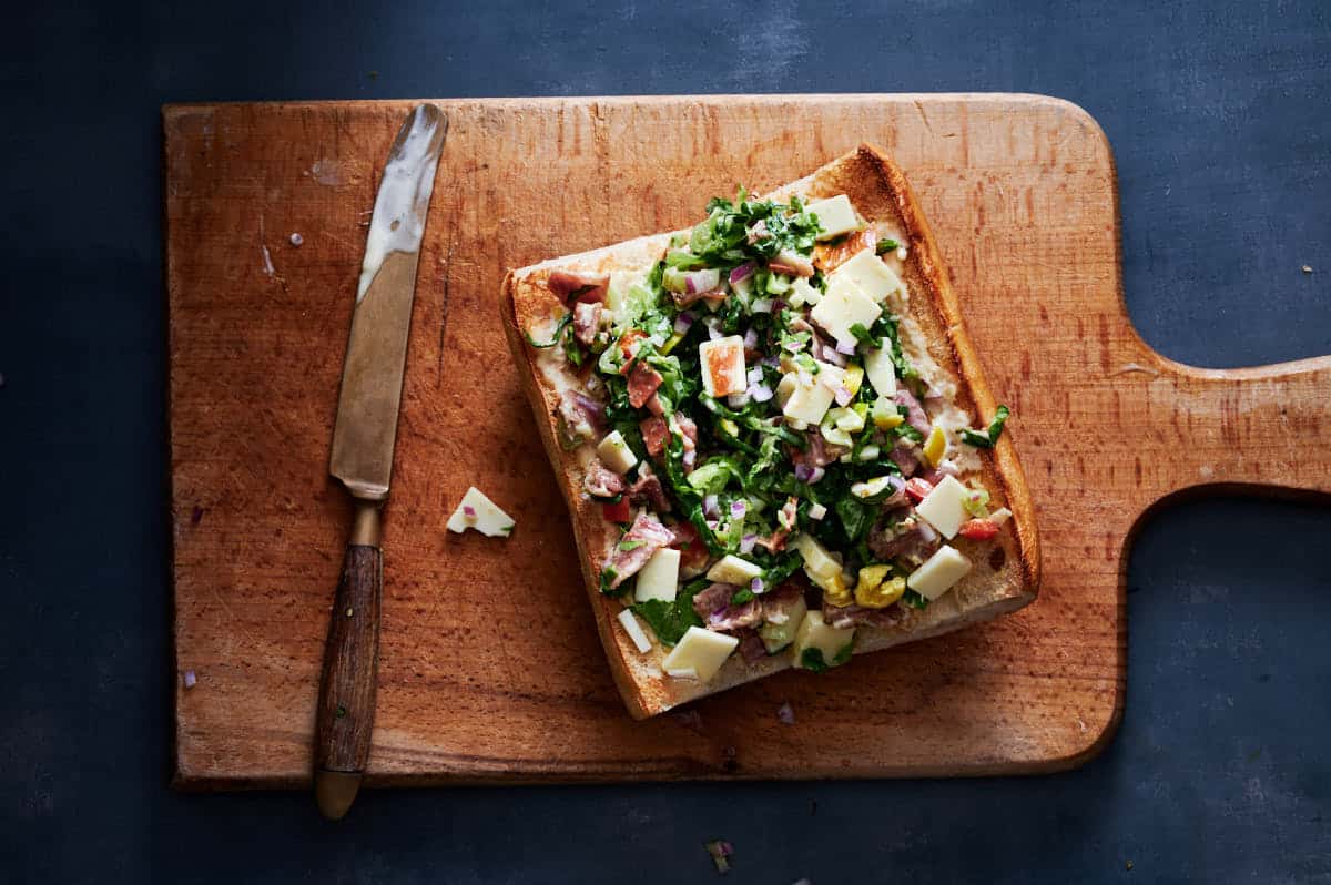 sandwich on a cutting board right before getting a drizzling thick balsamic glaze over the open faced chopped sandwich filling.