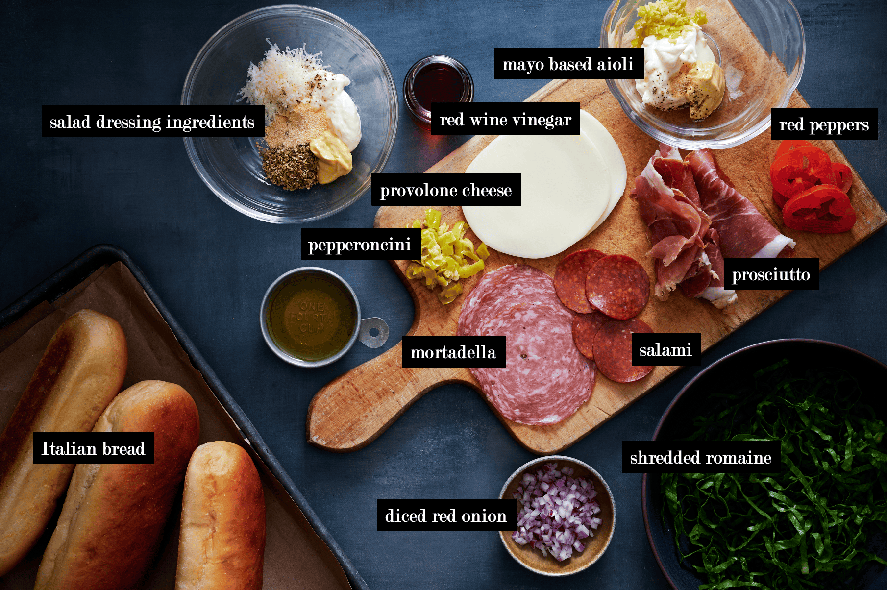 A table of chopped Italian sandwich ingredients, including deli meats, provolone cheese, red onions, lettuce, and pepperoncini.
