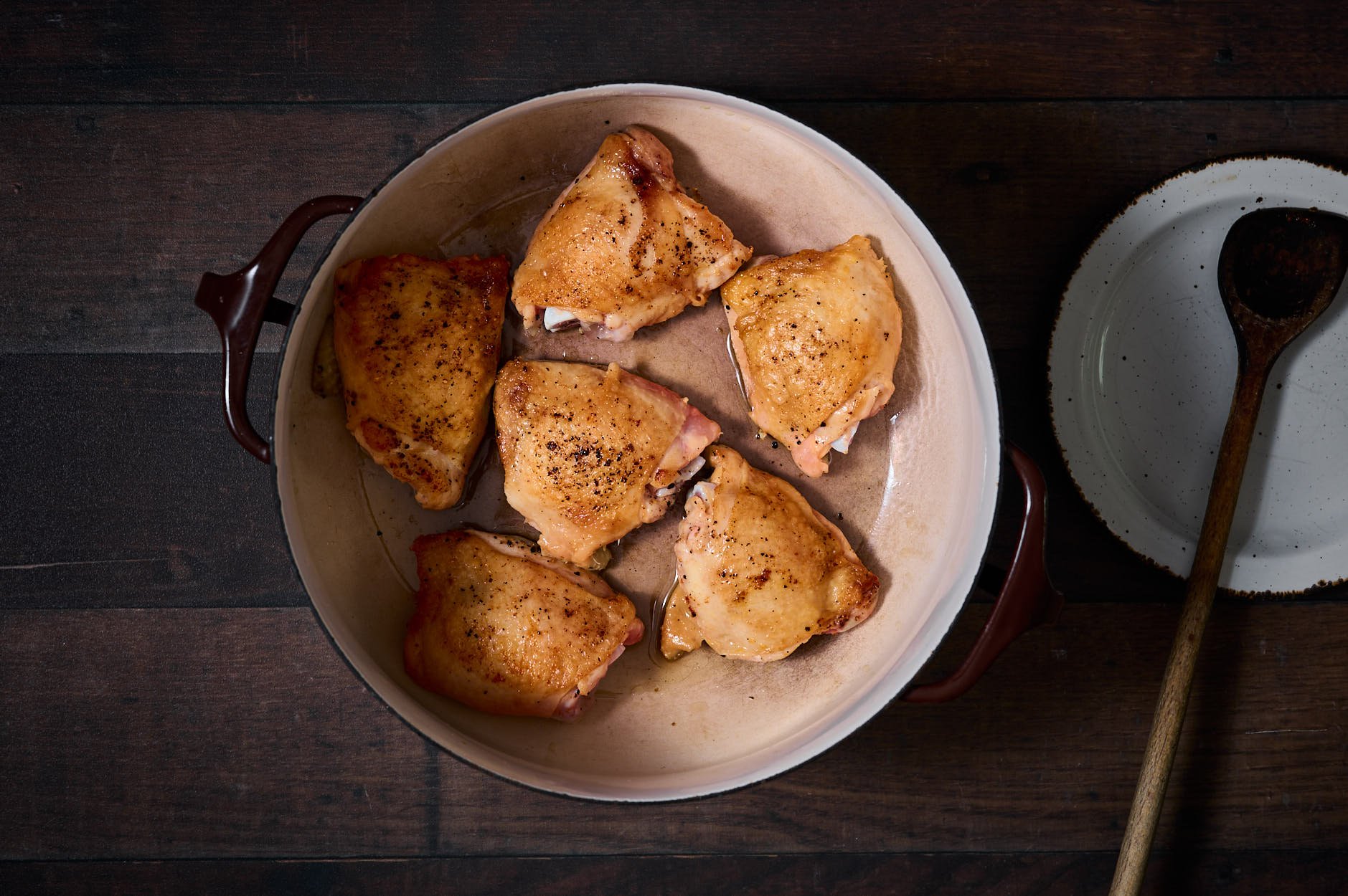 Seared chicken in a croc pot with a wooden sppon for Pollo alla cacciatora.