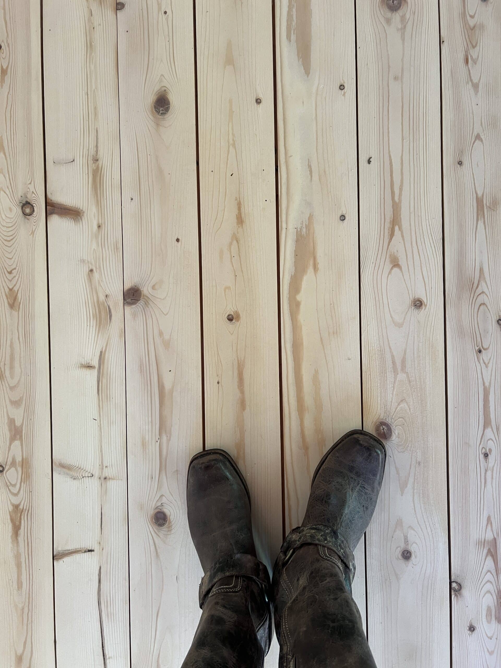 freshly sanded hardwood pine planks from a top down view with boots showing. 