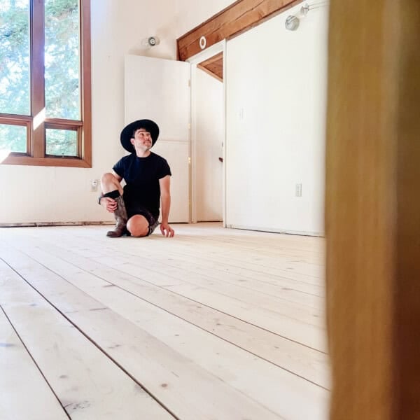 hardwood pine floors restoration, freshly sanded in an empty room with anthony sitting on it with a giant window. behind him.