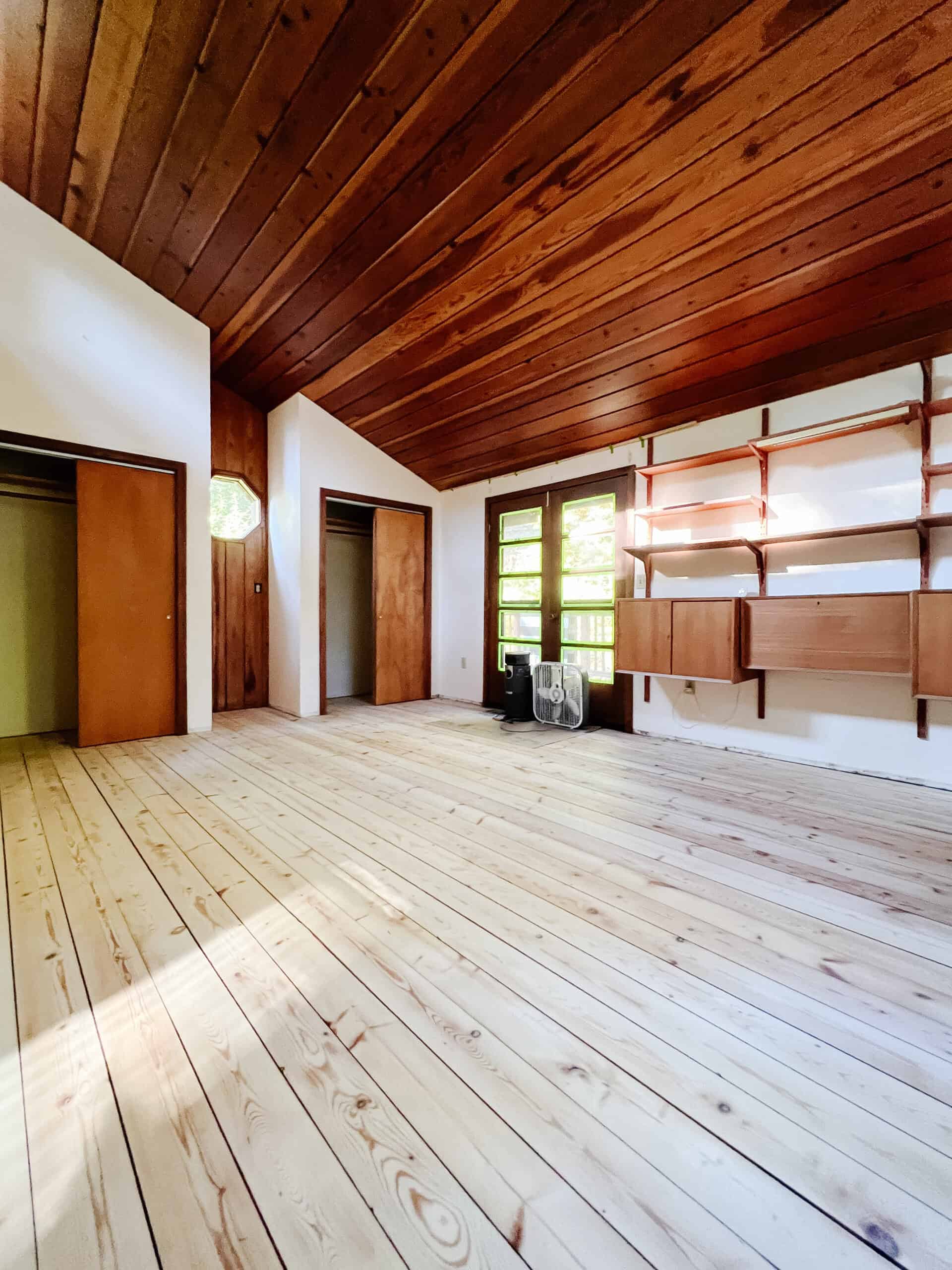 wide view of a loft bedroom that has pine floors that are sanded bright contrasting to dark redwood ceiling panels.