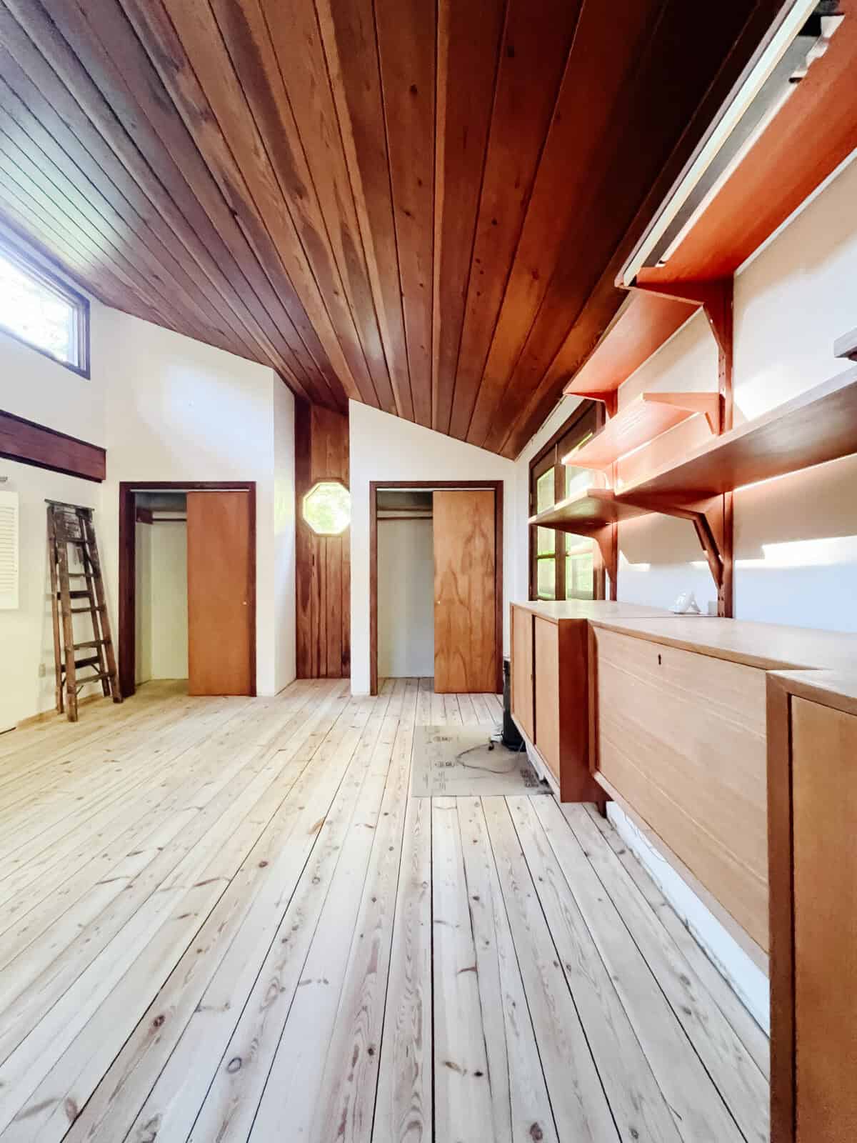 A cabin reno bedroom with a polygon window on redwood planks with new sanded pine floors.