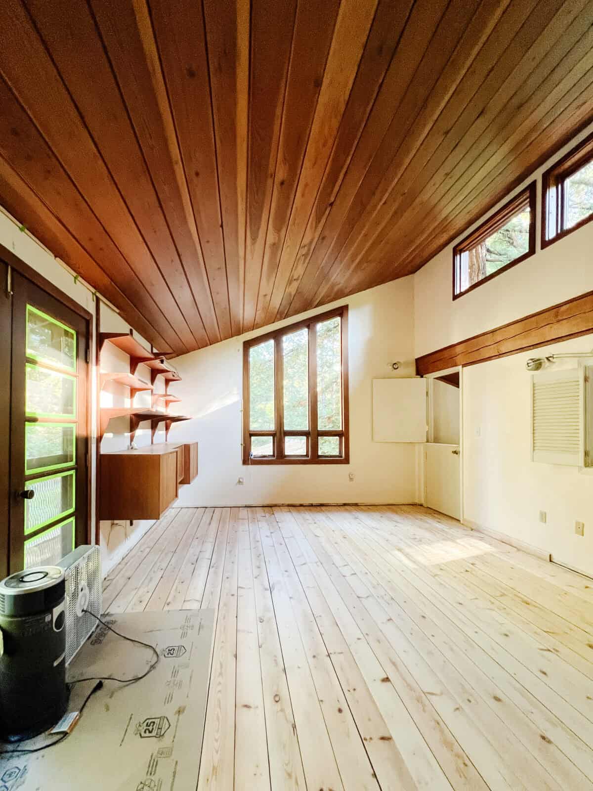 a full view of the cabin renovation with the baseboards removed, sanded pine floors, and a sealed redwood ceiling with fresh window trim.