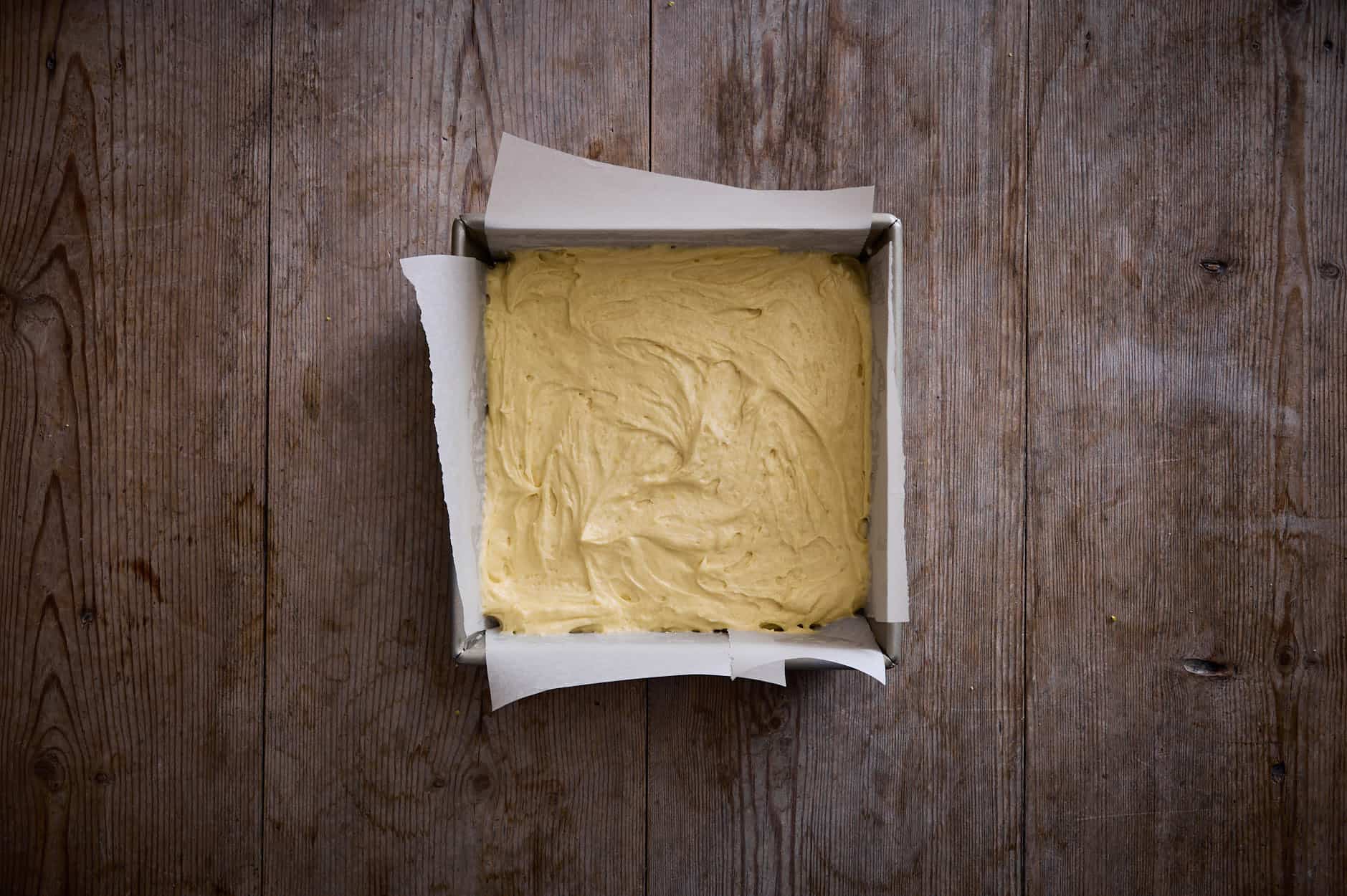 Batter for a lemon curd cake, swirled into a prepared tin with parchment paper, ready to bake. 