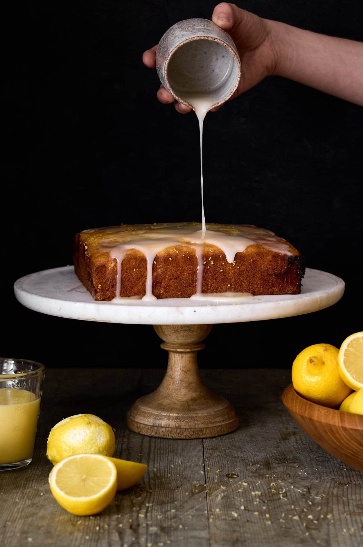 lemon curd cake with optional powdered sugar glaze on top of a marble cake stand on a farm table. 