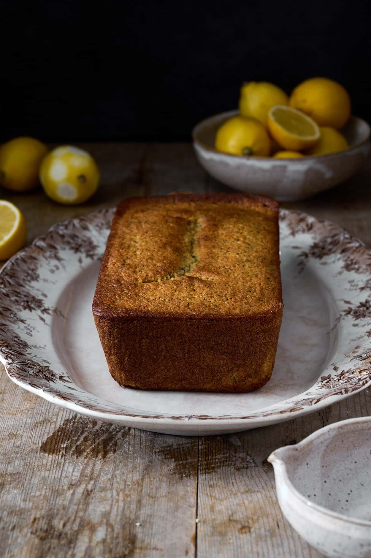 A freshly baked lemon poppy seed cake on a table with lemons cooling and ready to be glazed.