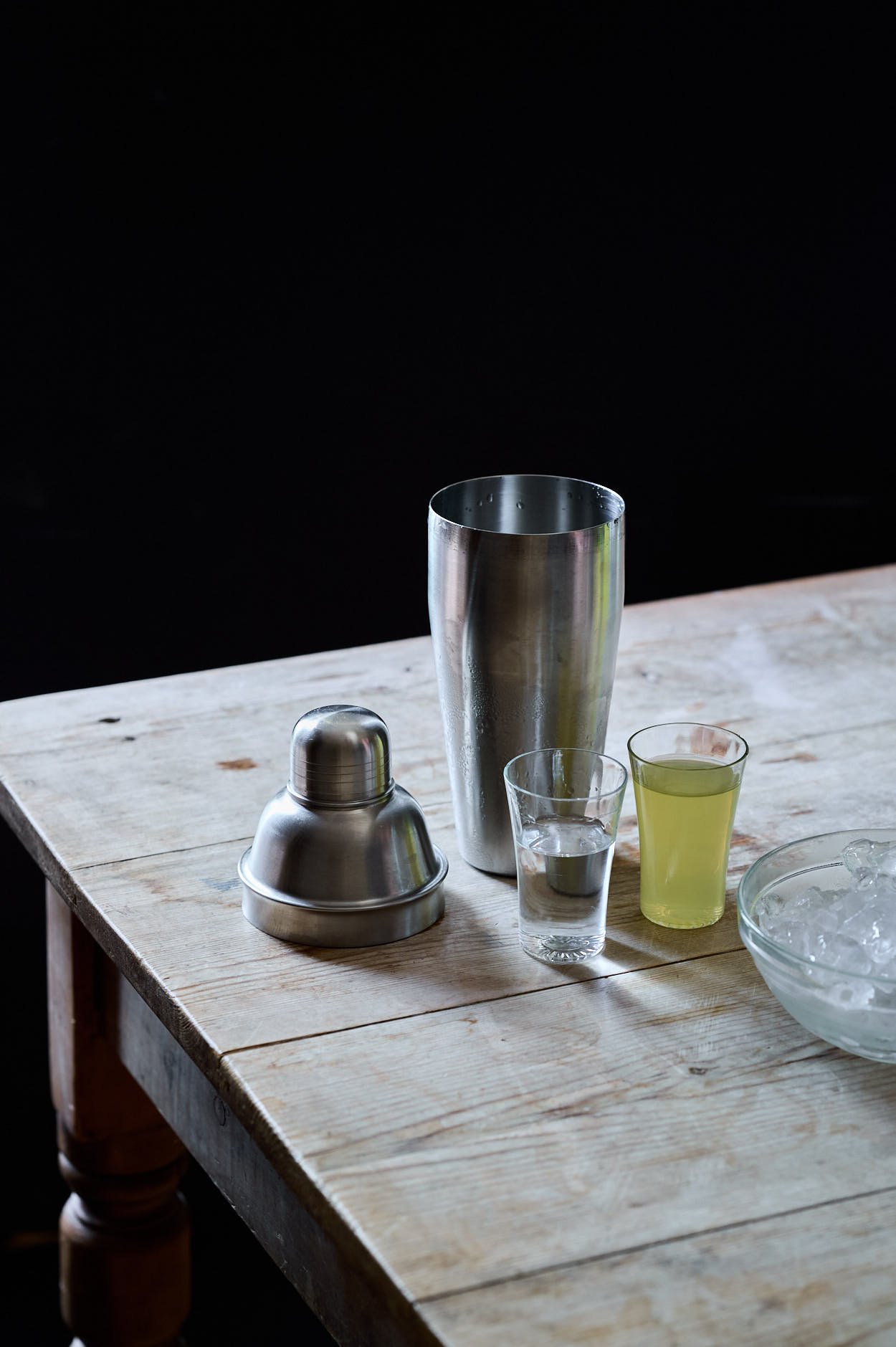 Lemoncello cocktail liquids on a wooden table, which include a shaker, vodka, and limoncello. 