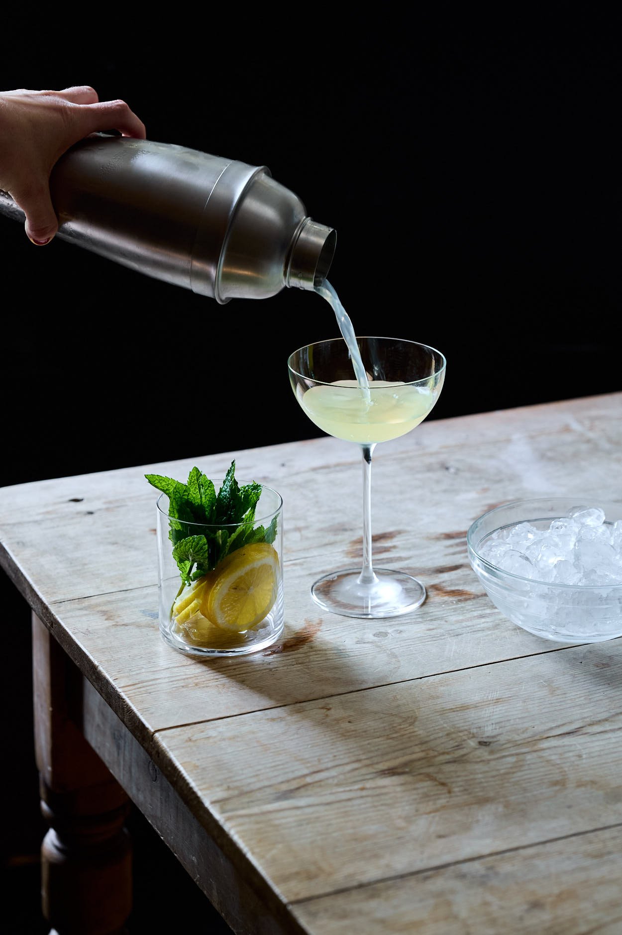 a shaker porung the Lemoncello cocktail into an upglass ready for mint and lemon garnish. 