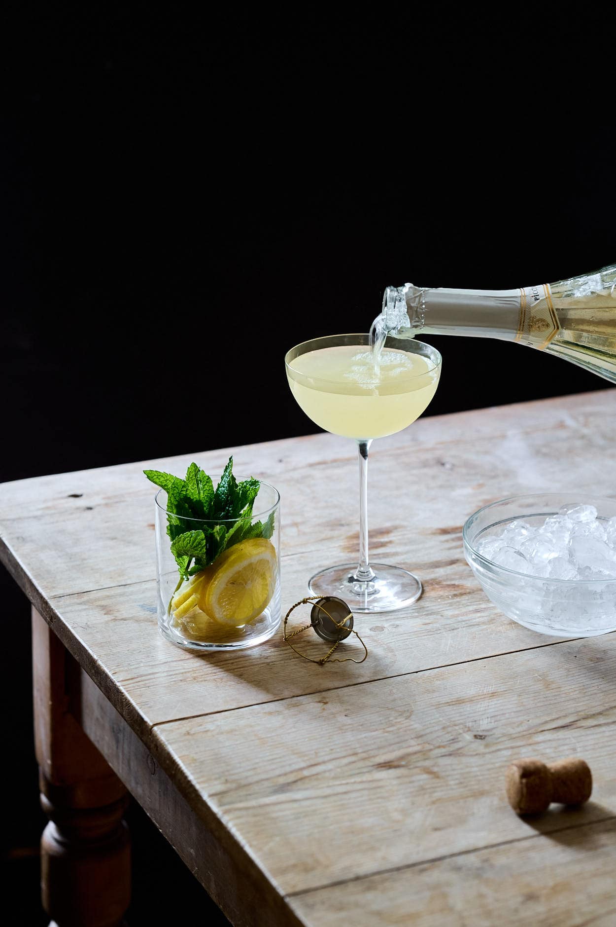 The Lemoncello cocktail being topped with a pout of bubbles in an up glass with the cork on the table. 